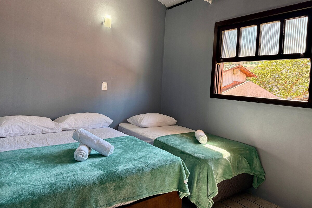 Una habitación con dos camas, una ventana con persianas y una lámpara fijada a la pared.