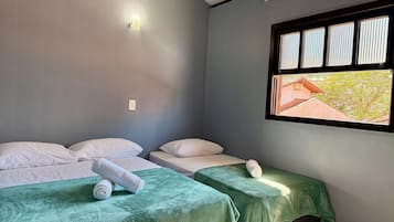 Una habitación con dos camas, una ventana con persianas y una lámpara fijada a la pared.
