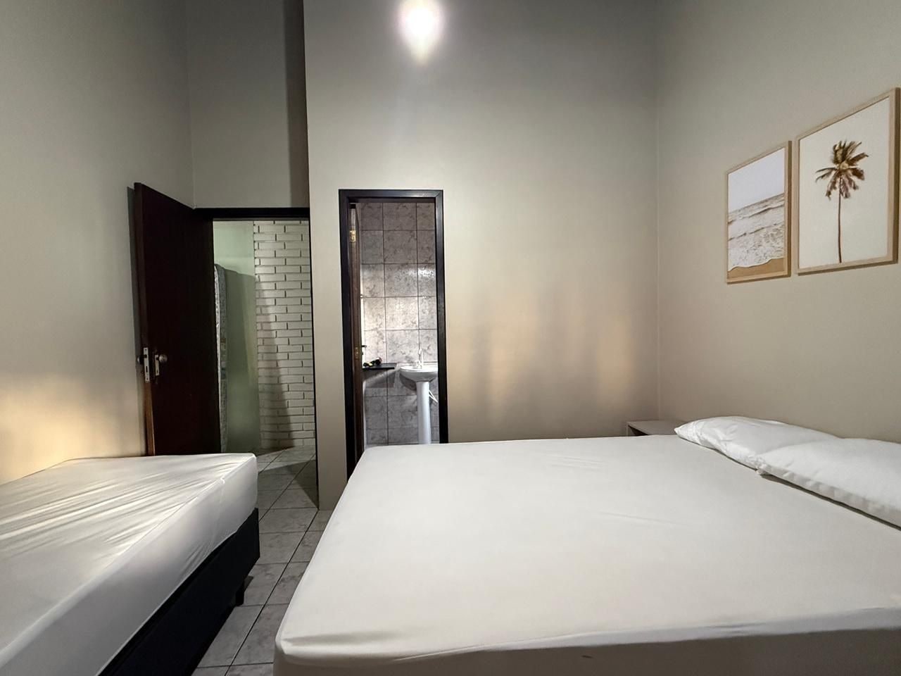 Een slaapkamer met twee bedden, een badkamer met betegelde wand en een deur naar een andere kamer.