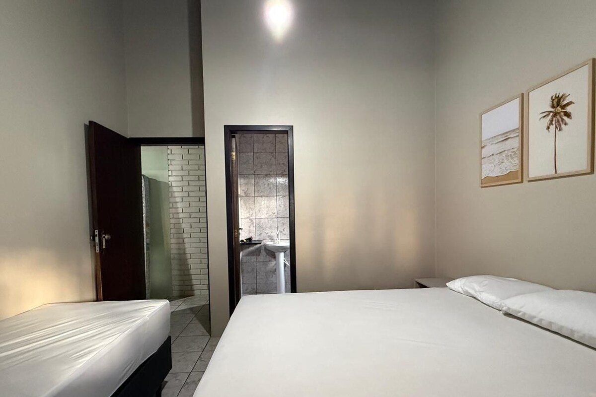 A bedroom with two beds, a bathroom with a tiled wall, and a door leading to another room.