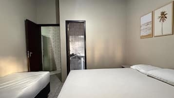 Een slaapkamer met twee bedden, een badkamer met betegelde wand en een deur naar een andere kamer.