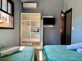 Quarto com duas camas, guarda-roupa, televisão e ar condicionado.
