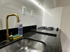 A modern kitchen with a stainless steel sink, a gold faucet, a gas stove, and a bottle of water.