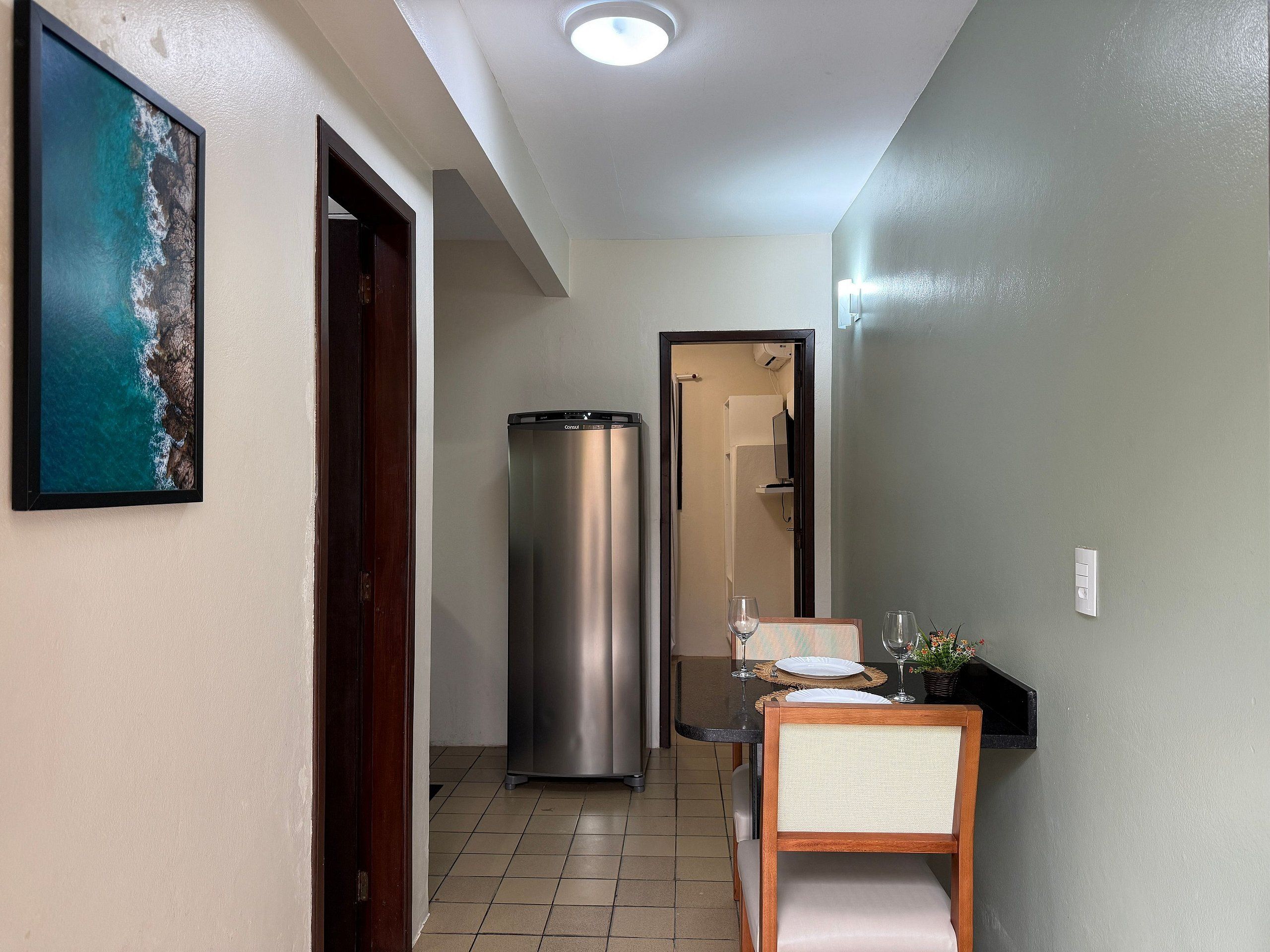 A hallway with a dining area, a refrigerator, and a framed picture of a coastal scene.