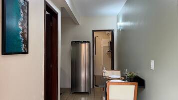 A hallway with a dining area, a refrigerator, and a framed picture of a coastal scene.