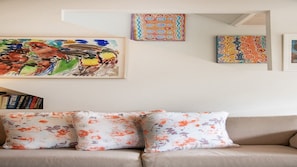 Uma sala de estar com um sofá bege, almofadas estampadas e três obras de arte emolduradas na parede.