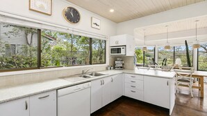 A modern kitchen with white cabinetry, a large window with a view of greenery, a microwave, and a coffee machine. - Bush setting and easy walk to beach (KILLCARE)
