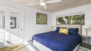 A bedroom with a bed, a ceiling fan, a window with a view of greenery, and a door leading to another room. - Bush setting and easy walk to beach (KILLCARE)