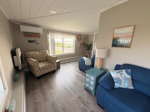 A cozy living room with a patterned armchair, a blue sofa, and a small side table with a lamp. - Beach Lovers Paradise!  Cozy 3 bedroom home steps from the beach.  (Fairhaven)