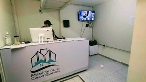 A reception desk with a logo, a computer, and a television mounted on the wall. - RESIDENCIA CASA BLANCA (Querétaro)