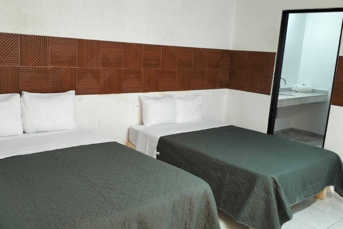 Quarto de hotel com duas camas de solteiro, cabeceira de madeira e um espelho grande.