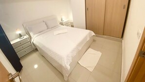 A bedroom with a bed, bedside tables, a nightstand, a wardrobe, and a bathroom door. - Apartamento Acogedor Cerca de la Playa (Boca Chica)