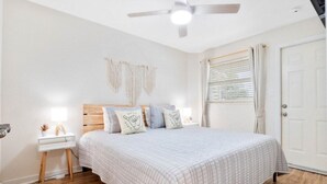 Un dormitorio con cama, mesita de noche, decoración en la pared y ventilador de techo.
