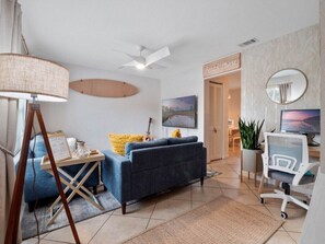 Ein modernes Wohnzimmer mit einer Couch, einem Schreibtisch, einem Sessel, einer Lampe und einem Gemälde.