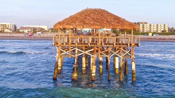 Un muelle de madera con una estructura de techo de paja, sostenida por múltiples pilares, que se adentra en el agua.