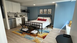 Une chambre d’hôtel compacte, dotée d’une kitchenette, d’un lit avec des oreillers rouges et d’un tapis aux couleurs vives.