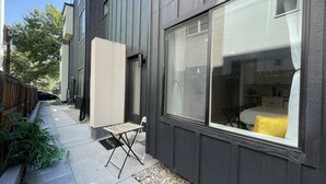 Un bâtiment moderne doté d’une grande fenêtre, d’un petit espace extérieur aménagé en coin salon et d’une clôture en bois.