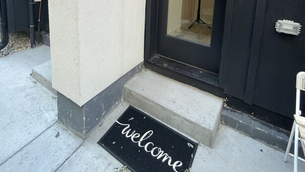 Une entrée moderne avec une porte noire, un paillasson et une petite marche menant à la porte.