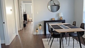 Ein moderner Essbereich mit dunklem Holzboden, Deckenventilator, rundem Spiegel und Esstisch mit schwarzen Stühlen.