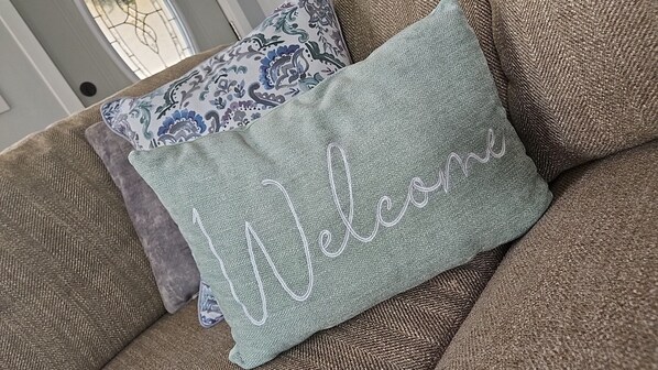 En sofa med en pude med et mønster og en grøn pude med broderet tekst 'Welcome'.