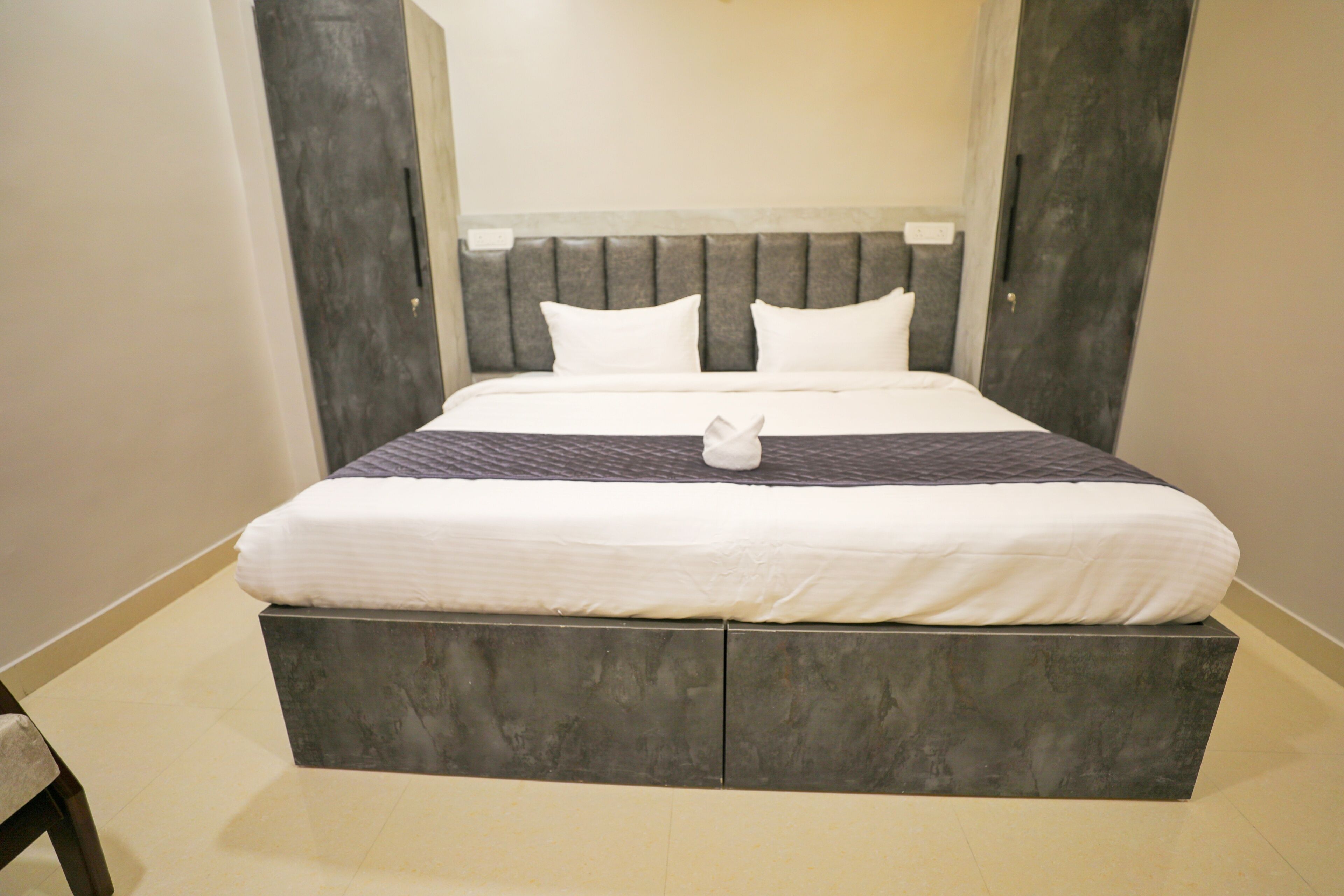 A neatly made bed with a white comforter and pillows, a grey headboard, and a grey platform bed base.