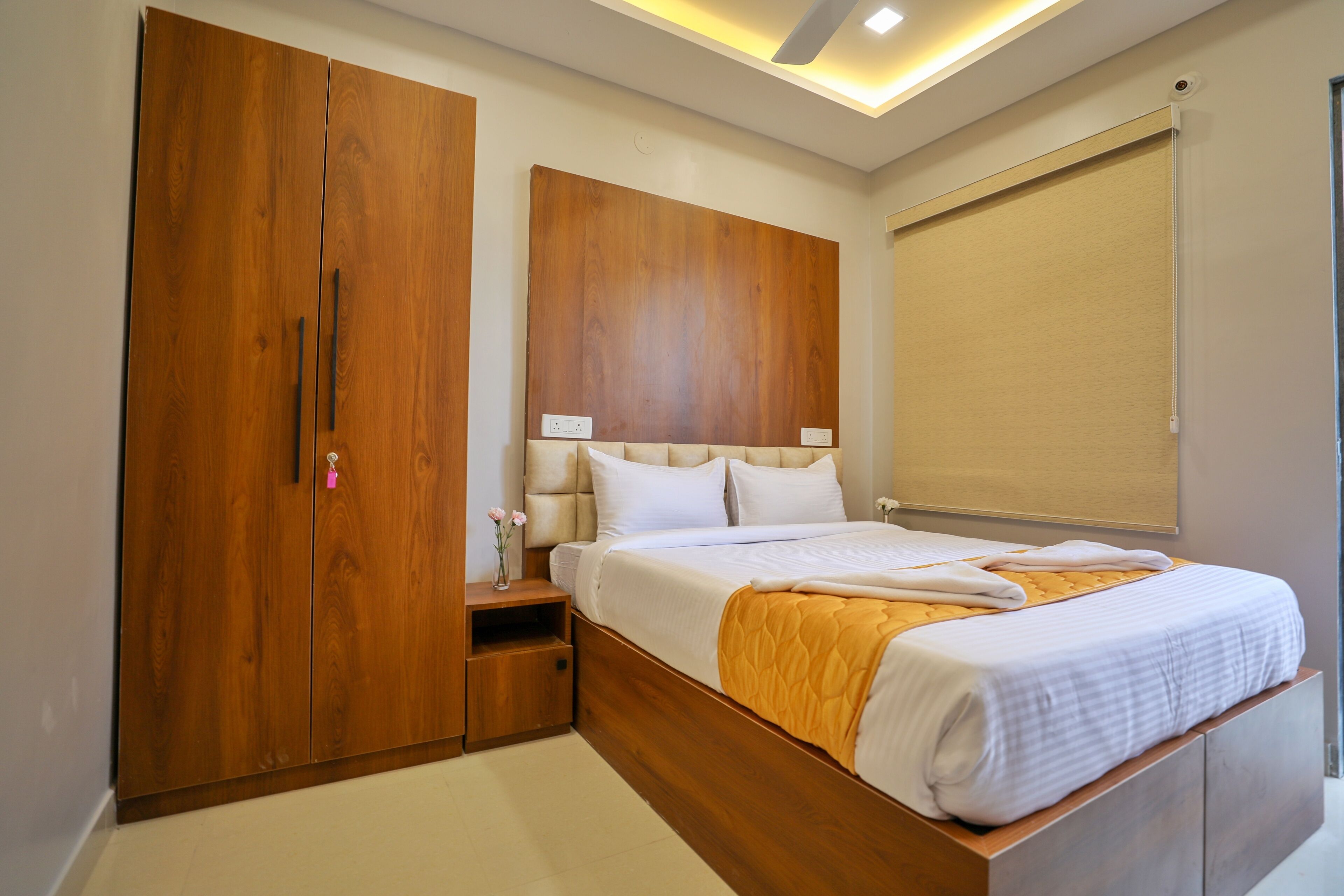 Een slaapkamer met een houten garderobe, een bed met een wit-oranje dekbed en een plafondlamp.