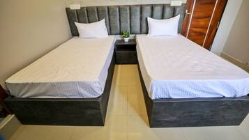 Habitación doble con una cama y cabecera oscura, ropa de cama blanca y una planta pequeña en la mesita de noche.