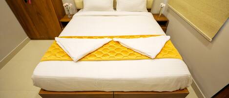 A neatly made bed with a yellow mattress cover and white linens, a wooden headboard, and a wooden nightstand with a vase of flowers.