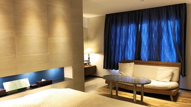 A hotel room with a bed, a small table, a sofa, and a nightstand.