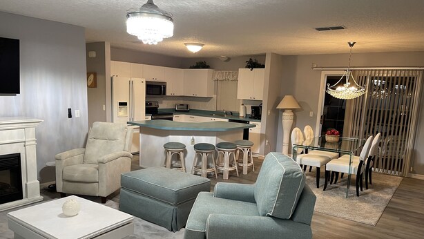 A modern living room with a fireplace, a dining area with a glass table, and a kitchen with a central island.