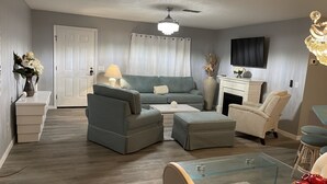 A living room with a grey sofa, two armchairs, a glass coffee table, and a fireplace.