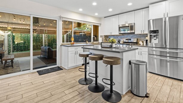 Una cocina moderna con armarios blancos, electrodomésticos de acero inoxidable y una zona con taburetes de bar.