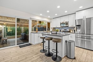 A modern kitchen with white cabinets, stainless steel appliances, and a bar stool area.