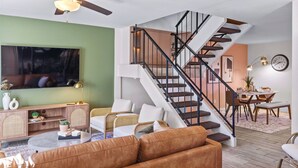 Una sala de estar moderna con escalera, televisor y comedor.