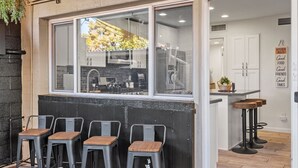 Una cocina con un ventanal amplio, tres taburetes de bar y una pequeña isla con taburetes.