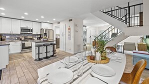 Una cocina moderna con armarios blancos, electrodomésticos de acero inoxidable y una isla central con taburetes de bar.