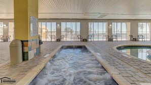 Área interna da piscina com um elemento aquático central, assentos ao redor e grandes janelas com vista.