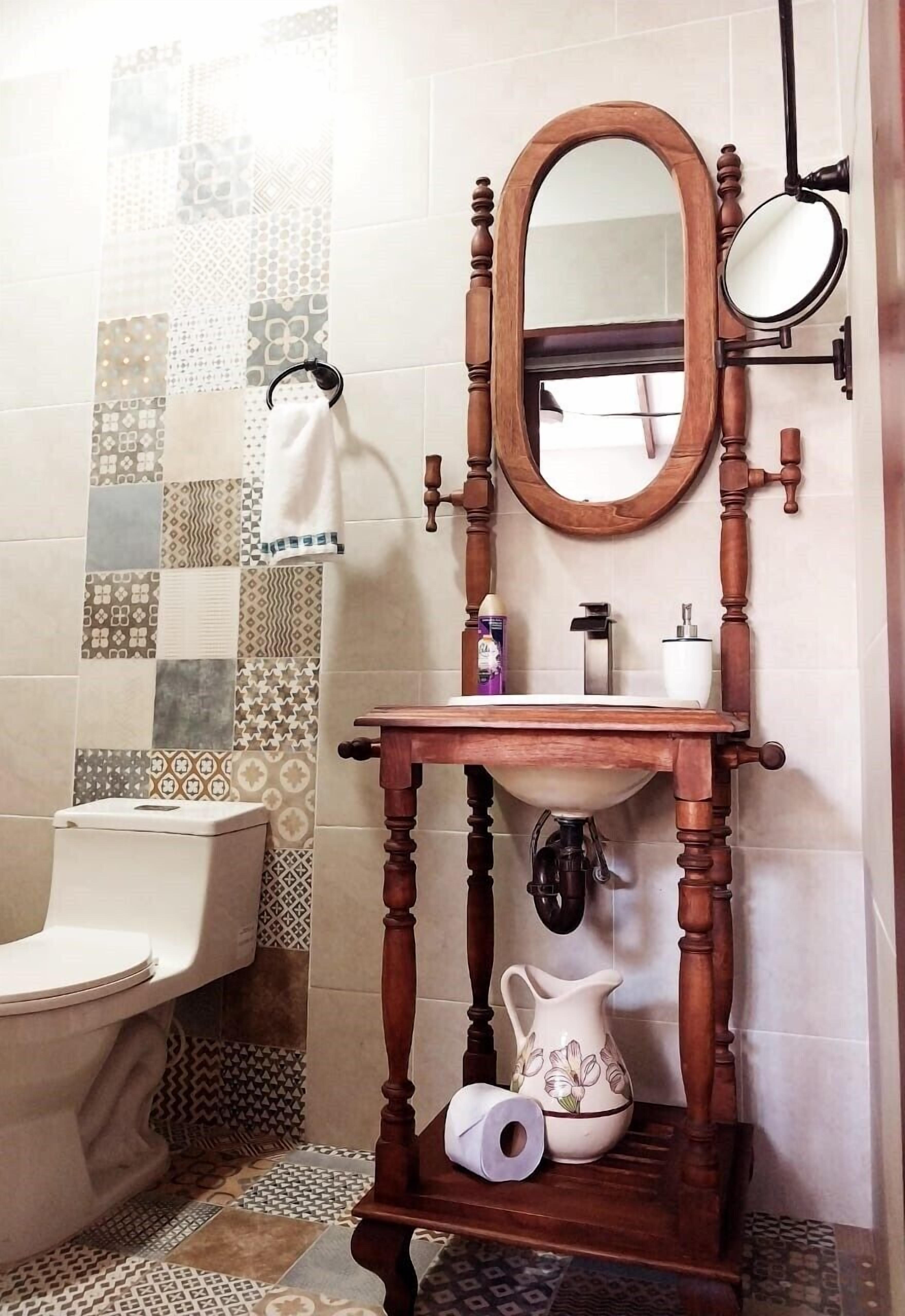 Un baño con tocador de madera, lavamanos, espejo y retrete.
