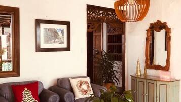 Un soggiorno con soffitto alto, travi in legno, un lampadario, un divano con un cuscino a tema natalizio, un tavolo con un libro e un mobile contenente oggetti decorativi.