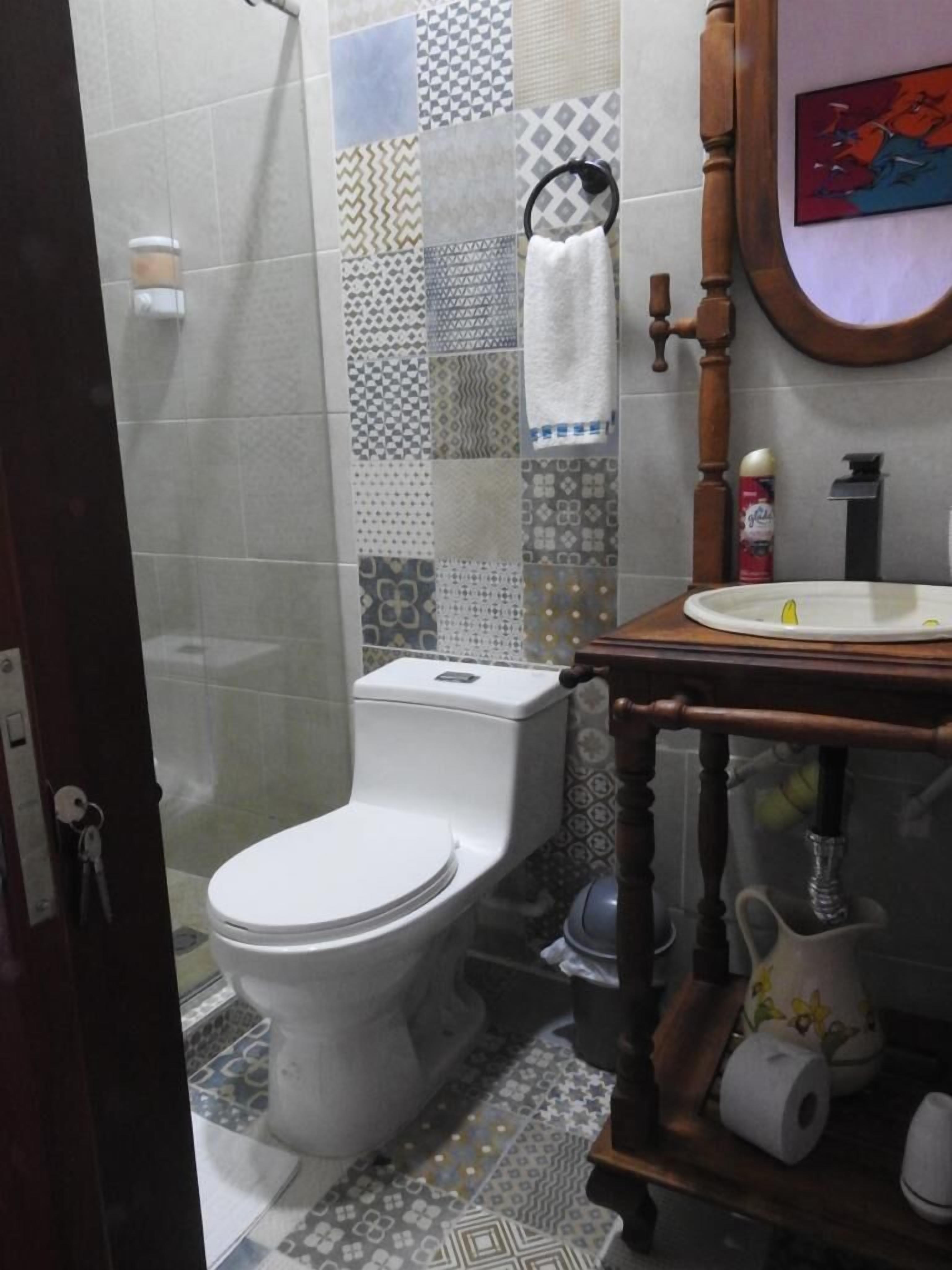 A bathroom with a toilet, a sink with a mirror, and a shower area.
