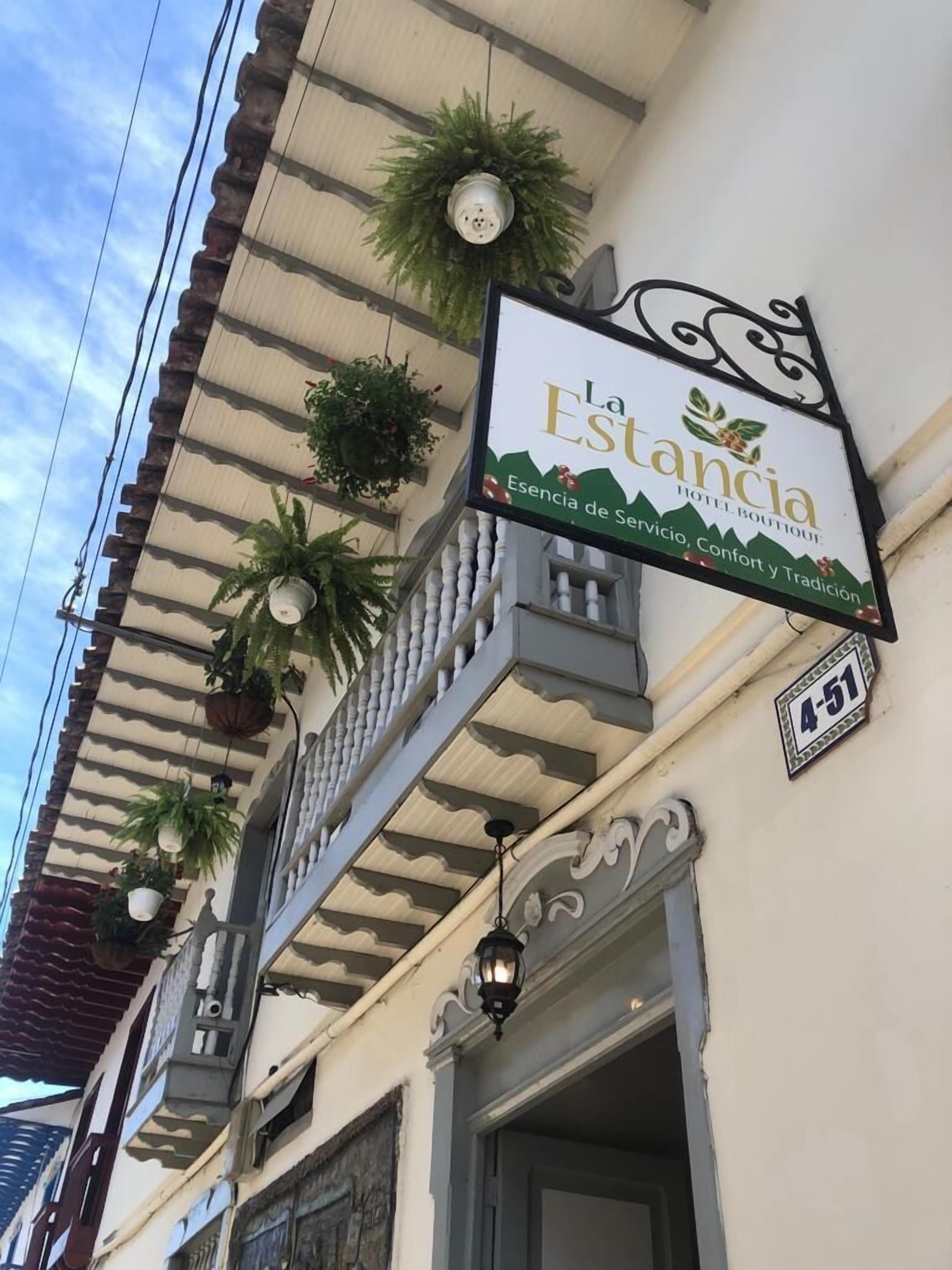 Señal de hotel con el nombre 'La Estancia Hotel Boutique' y un balcón con plantas en macetas.