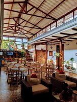 Amplio espacio interior con mesas y sillas de madera, una escalera y una variedad de plantas en macetas.