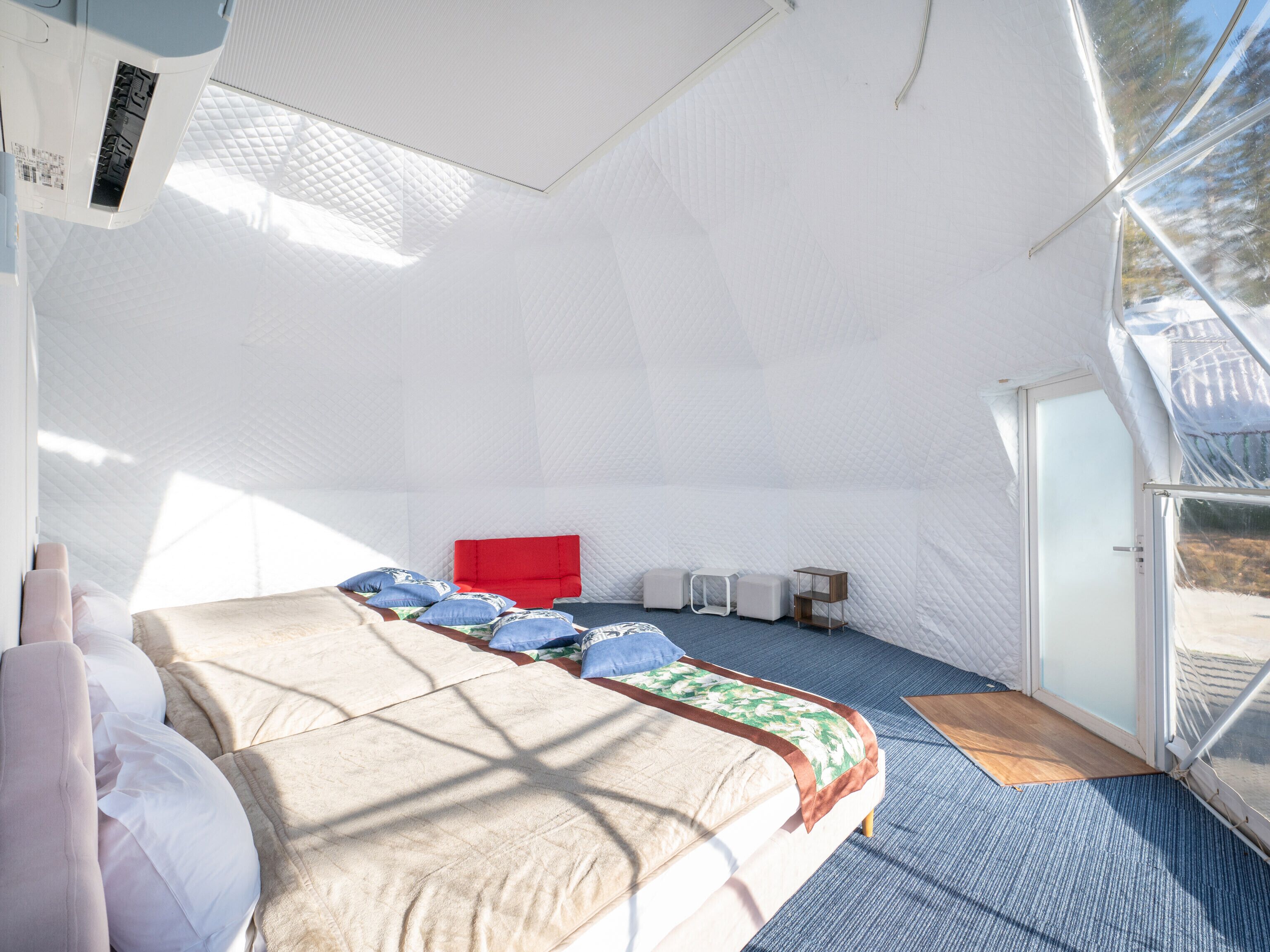 A spacious, well-lit room with a large bed, a red headboard, and a seating area with small tables and chairs.