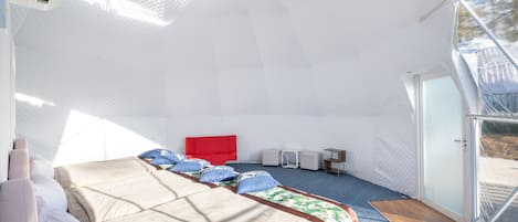 A spacious, well-lit room with a large bed, a red headboard, and a seating area with small tables and chairs.
