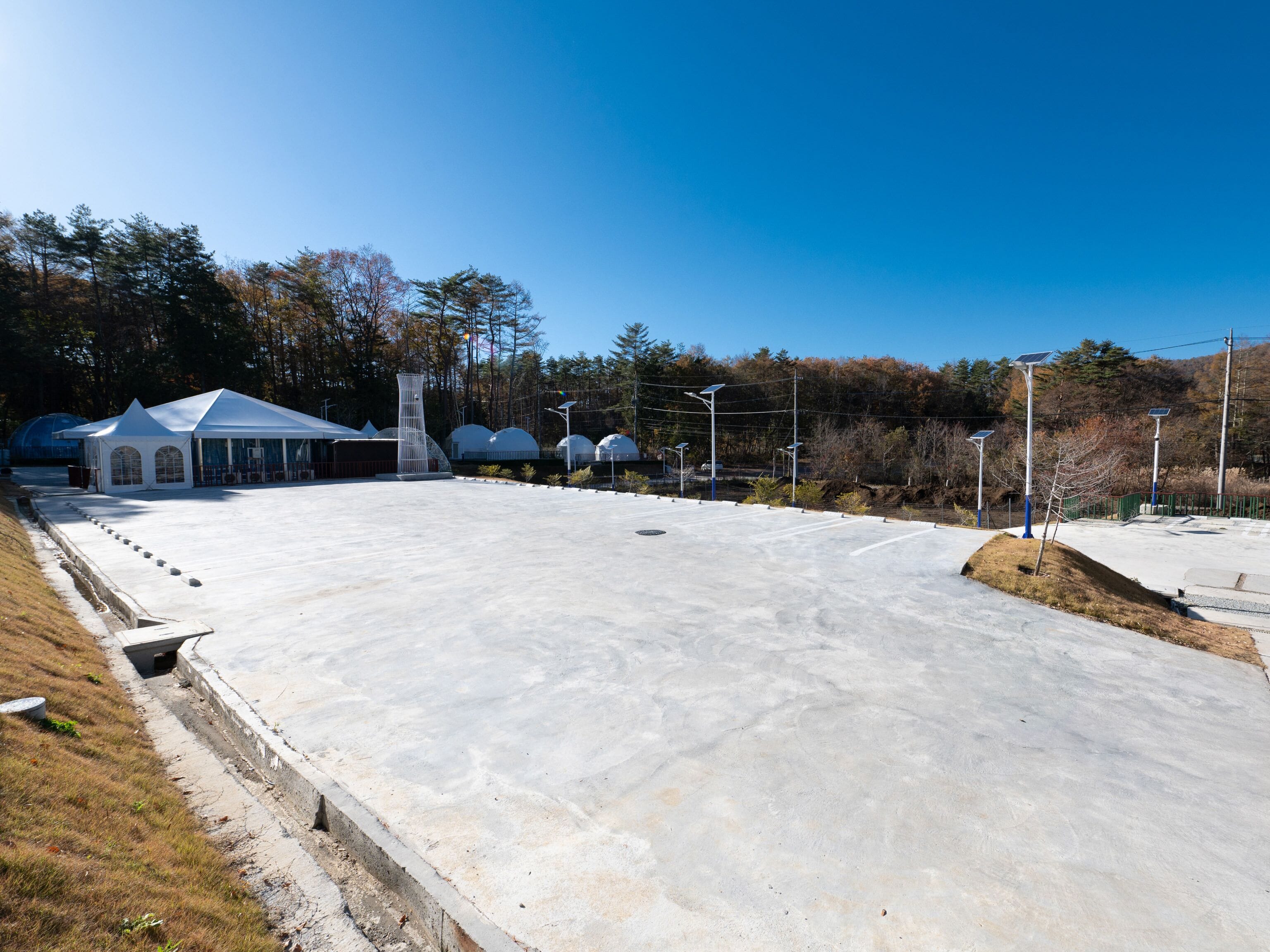 A large, open concrete area with a white pavilion and solar street lamps.