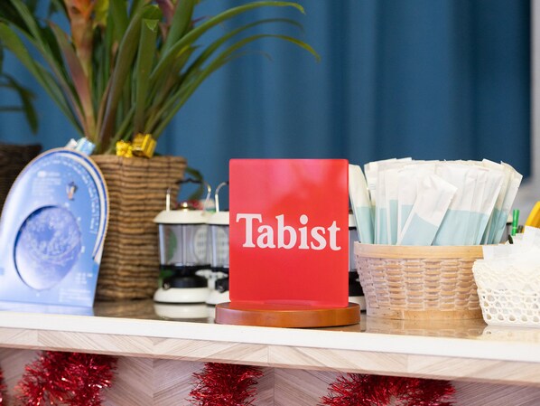 A desk with a red 'Tabist' sign, a blue clock, a white kettle, and a basket of tissues. - Fuji Hoshizorano Mura Tabist (Narusawa)