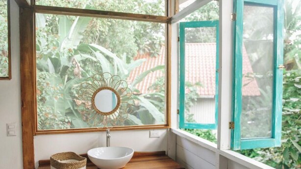A bathroom with a white sink, a mirror, and a window with a teal frame. - CASA BOHÖ (Cahuita)