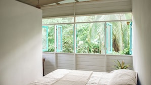 A bedroom with a bed, a window with a view of greenery, and a ceiling with wooden beams. - CASA BOHÖ (Cahuita)
