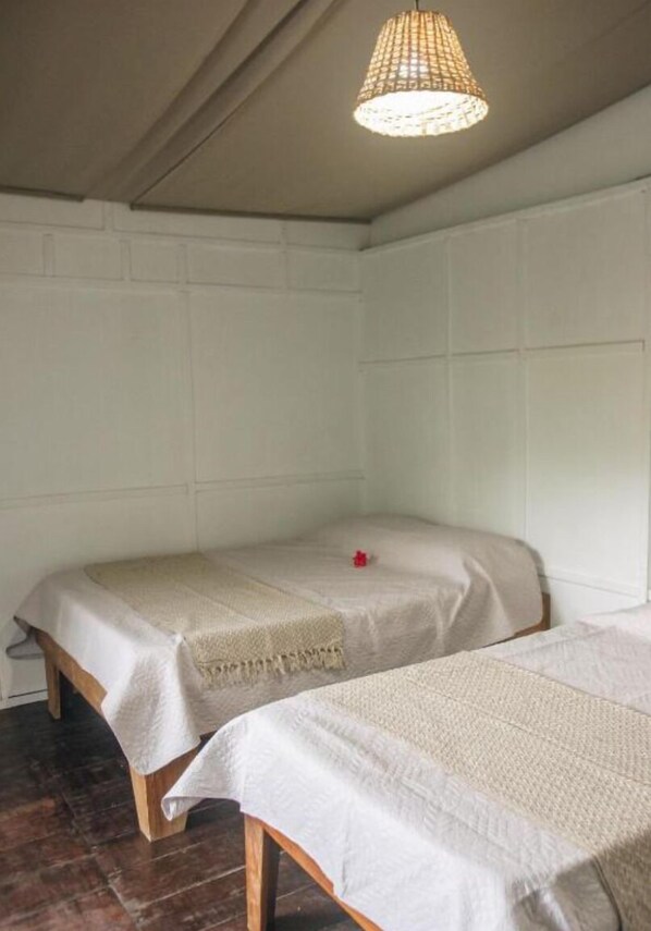 Une petite chambre accueillante avec deux lits simples, un plancher en bois et un luminaire suspendu.