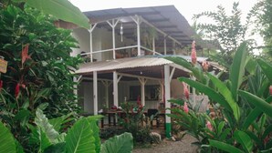 A two-story building with a covered patio area, surrounded by lush tropical vegetation. - CASA BOHÖ (Cahuita)